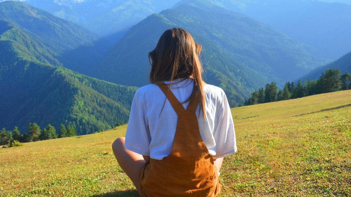 A woman sitting on top of a lush green hillside